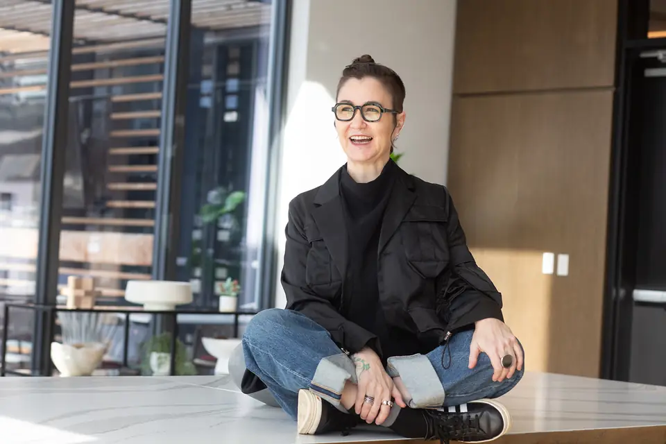 Sarah Novotny, sitting cross-legged on a table, laughing