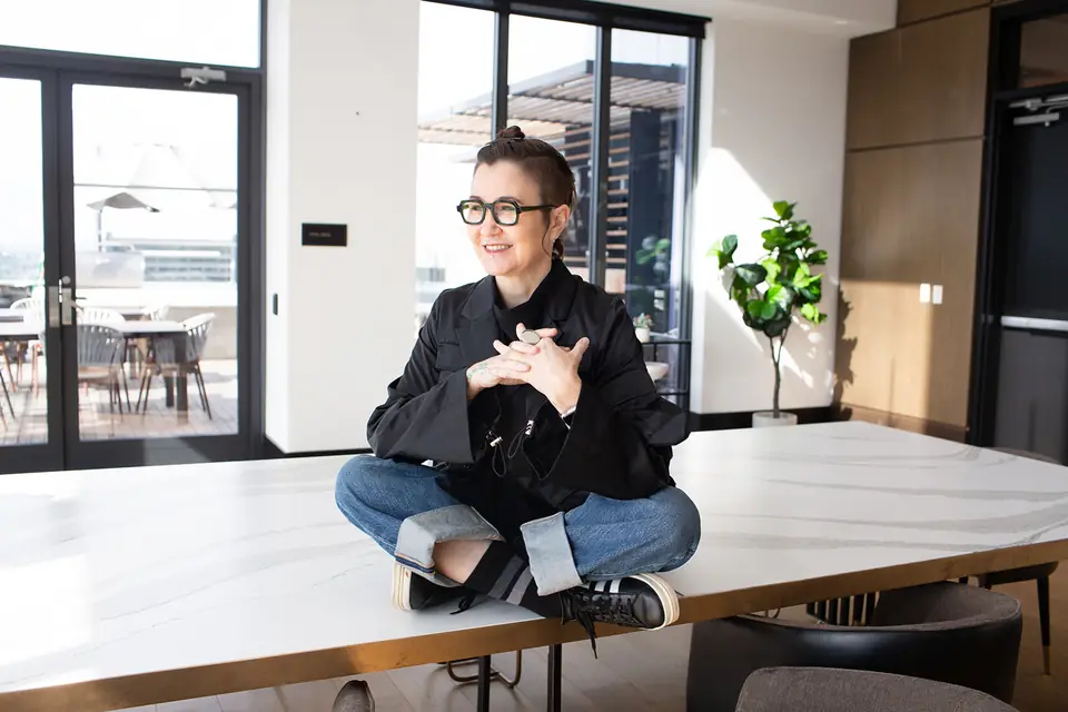 Sarah Novotny, sitting cross-legged on a conference-room table, smiling